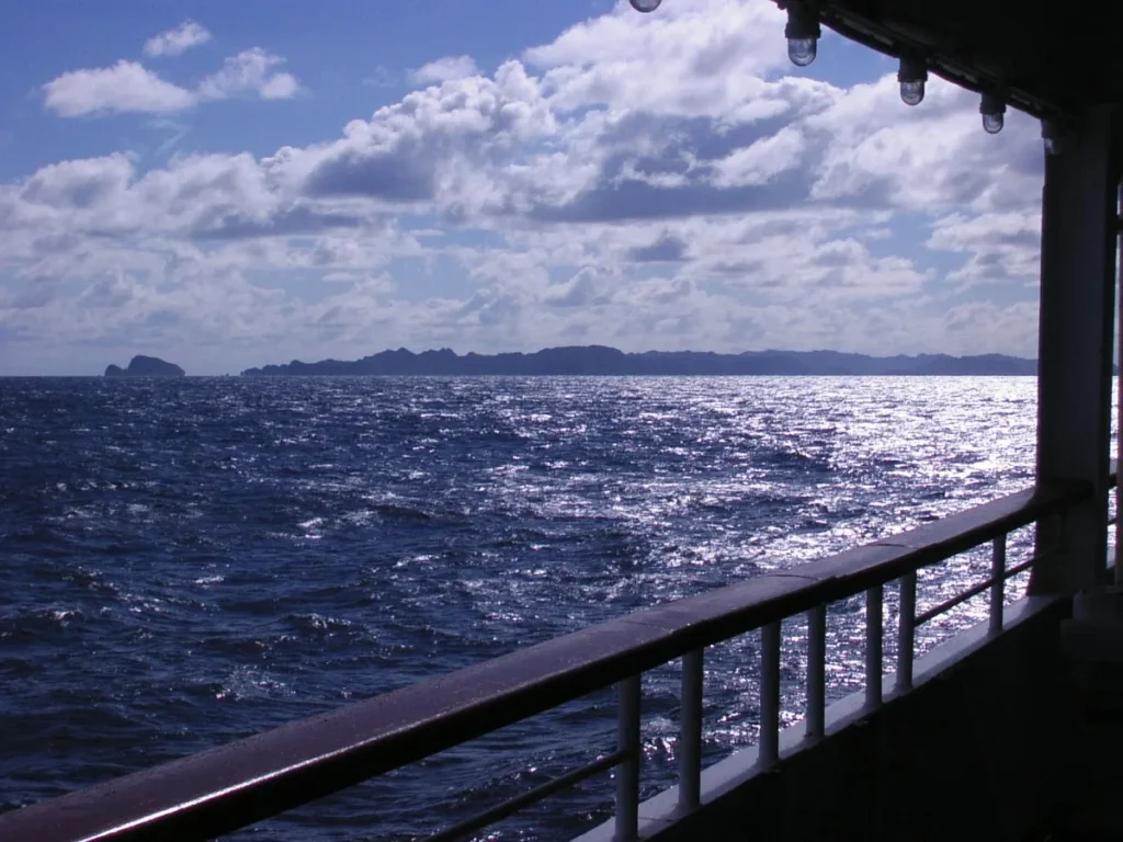 おがさわら丸のデッキから眺める輝く海とケータ諸島のシルエット。12月なのに夏を思わせる空。