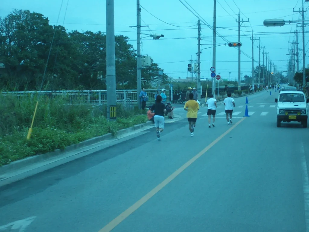 冬の石垣島の風物詩、石垣島マラソン。沿道の緑と広い空の下、自分のペースでゴールを目指すランナーたち。路線バスも減速で応援。
