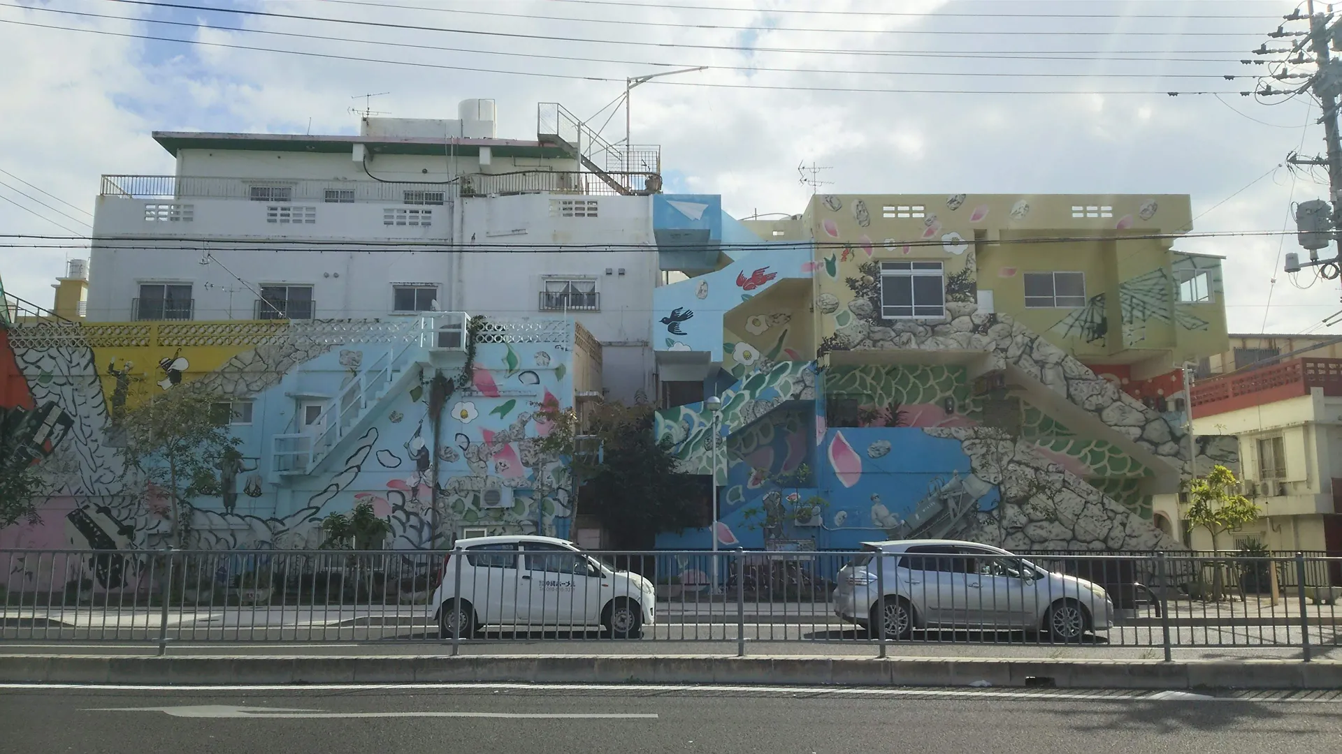沖縄市コザの街中にある、パステルカラーの装飾と鳥や花の絵が描かれた建物の外階段
