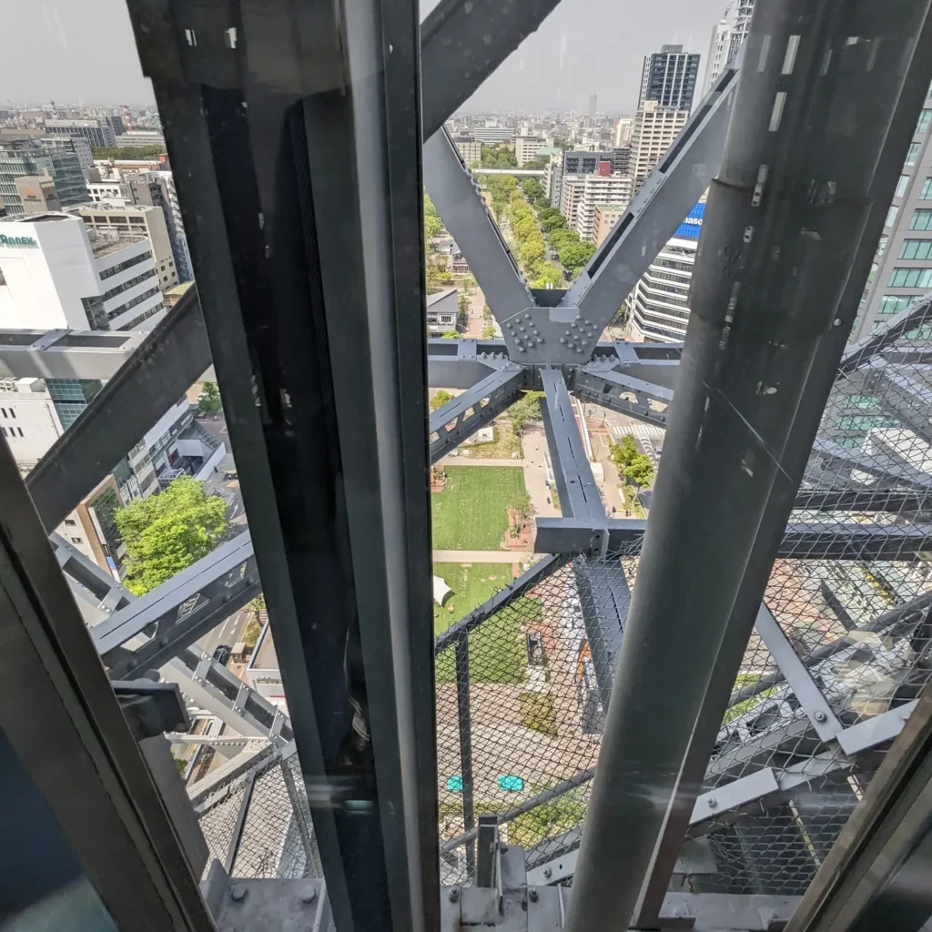 テレビ塔のエレベーター。一部ガラス張りで鉄骨と地上が見えるスリルある光景
